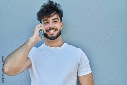 Young hispanic man smiling confident talking on the smartphone over white isolated background