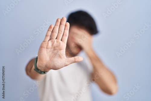 Hispanic man with beard standing over white background covering eyes with hands and doing stop gesture with sad and fear expression. embarrassed and negative concept.