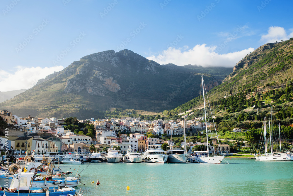 View of Castellammare del Golfo town, Sicily island, Italy. Beautiful mediterranean port with fishing boats and yachts over old town and mountain background. Popular travel destination in Europe