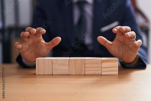 Young latin man business worker sitting on table with wooden cubes at office