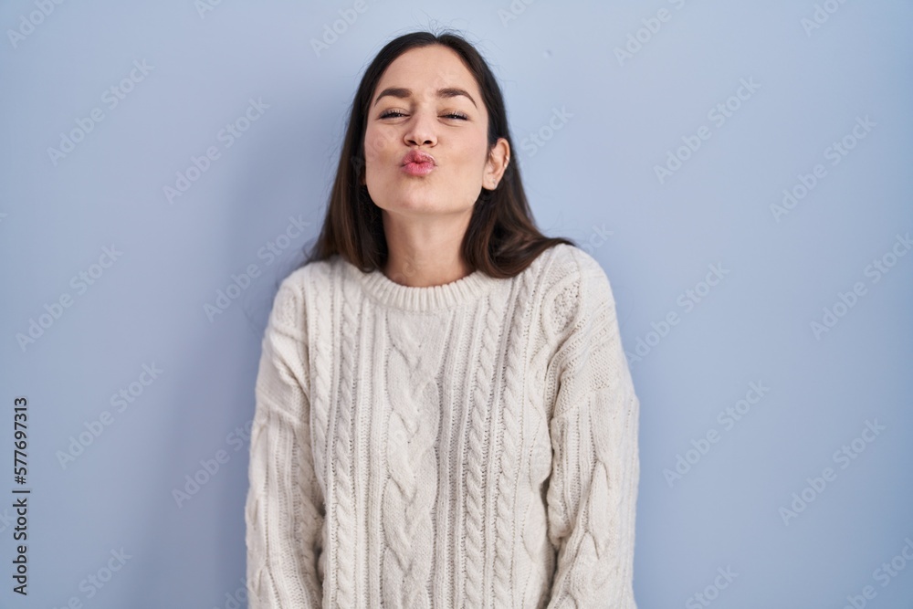 Young brunette woman standing over blue background looking at the camera blowing a kiss on air being lovely and sexy. love expression. Young brunette woman standing over blue background looking at the camera blowing a kiss on air being lovely and sexy. love expression.