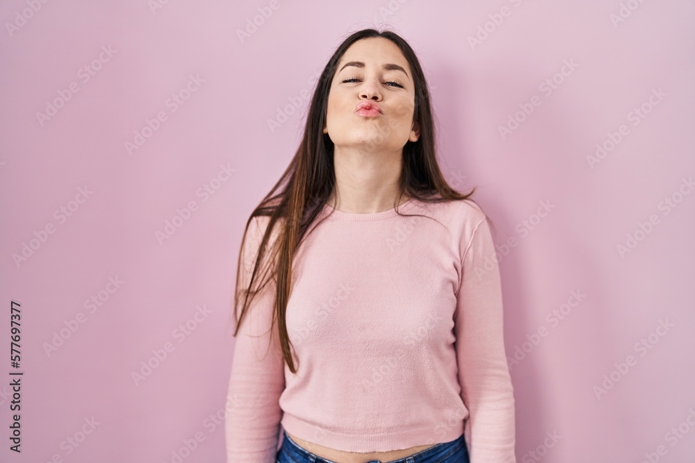 Young brunette woman standing over pink background looking at the camera blowing a kiss on air being lovely and sexy. love expression. Young brunette woman standing over pink background looking at the camera blowing a kiss on air being lovely and sexy. love expression.