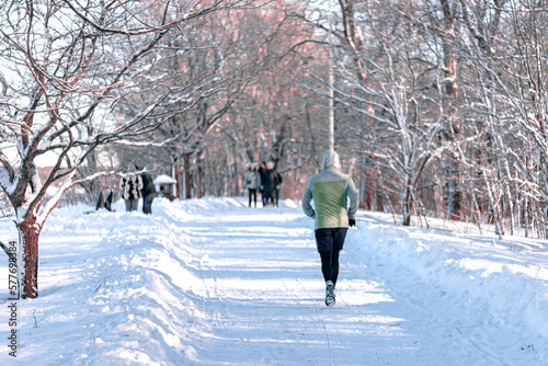 A man in sportswear runs along the road in a winter park