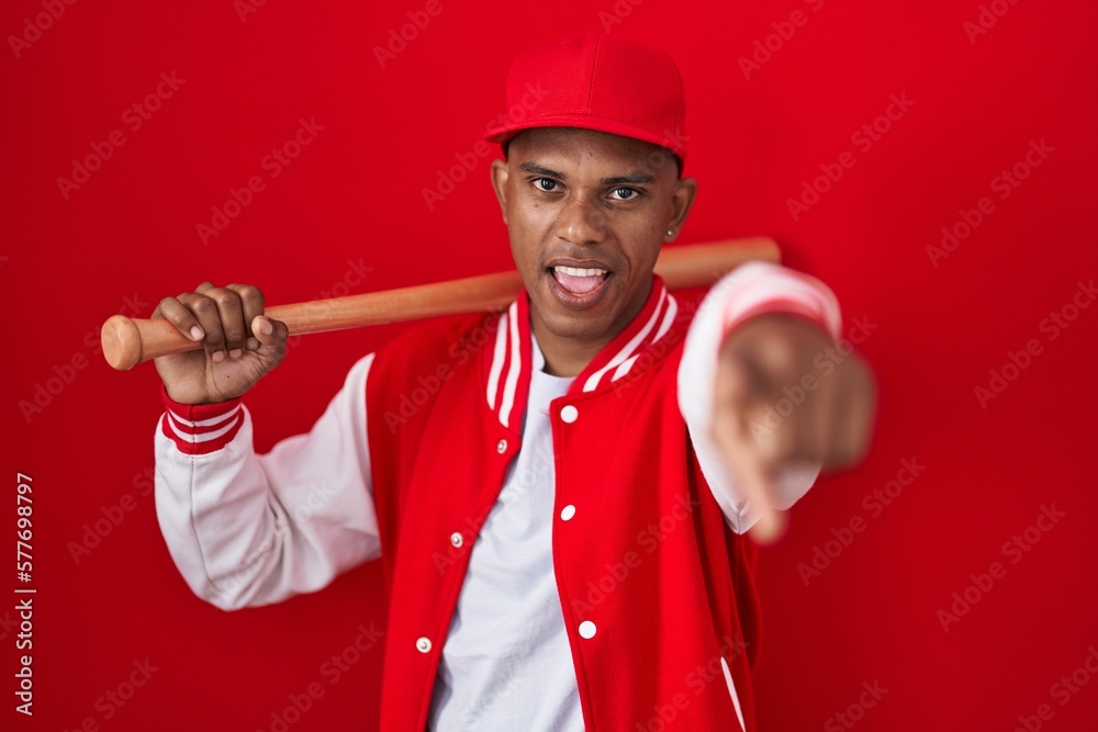 Young hispanic man playing baseball holding bat pointing displeased and frustrated to the camera, angry and furious with you