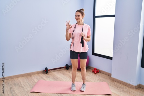 Young hispanic girl training doing ok sign with fingers, smiling friendly gesturing excellent symbol