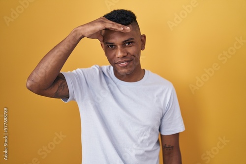 Young hispanic man standing over yellow background worried and stressed about a problem with hand on forehead, nervous and anxious for crisis