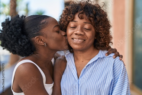 African american women mother and daughter hugging each other kissing at street