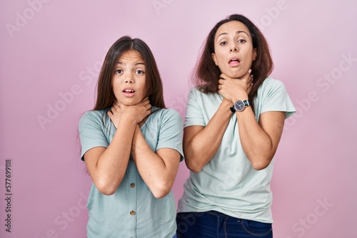 Young mother and daughter standing over pink background shouting suffocate because painful strangle. health problem. asphyxiate and suicide concept.