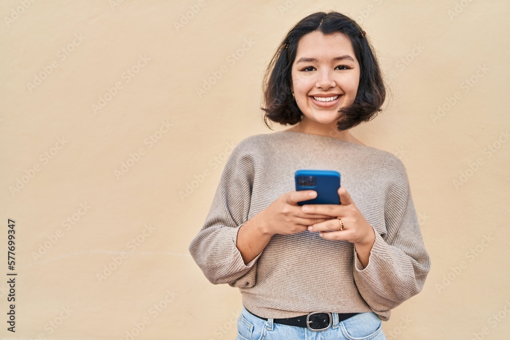 Young woman smiling confident using smartphone over yellow background Young woman smiling confident using smartphone over yellow background
