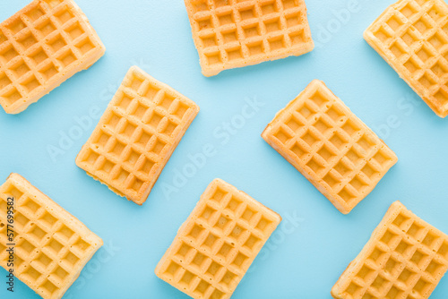 Fresh golden waffles on light blue table background. Pastel color. Closeup. Sweet snacks pattern. Top down view.