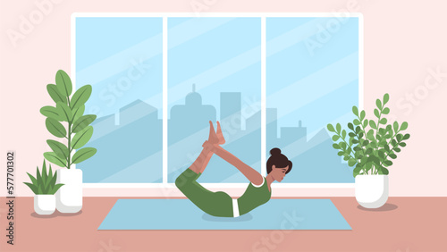 A woman in sportswear performs a yoga bow pose while lying on a mat in a room. The concept of a healthy lifestyle in a big city.