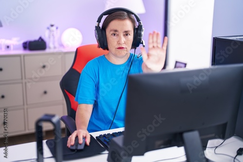 Middle age hispanic woman playing video games with open hand doing stop sign with serious and confident expression, defense gesture