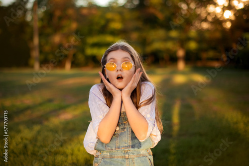 surprised and excited school girl on lawn with green trees background
