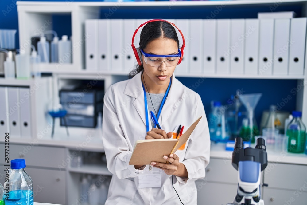 Young african american woman scientist listening to music write on book at laboratory