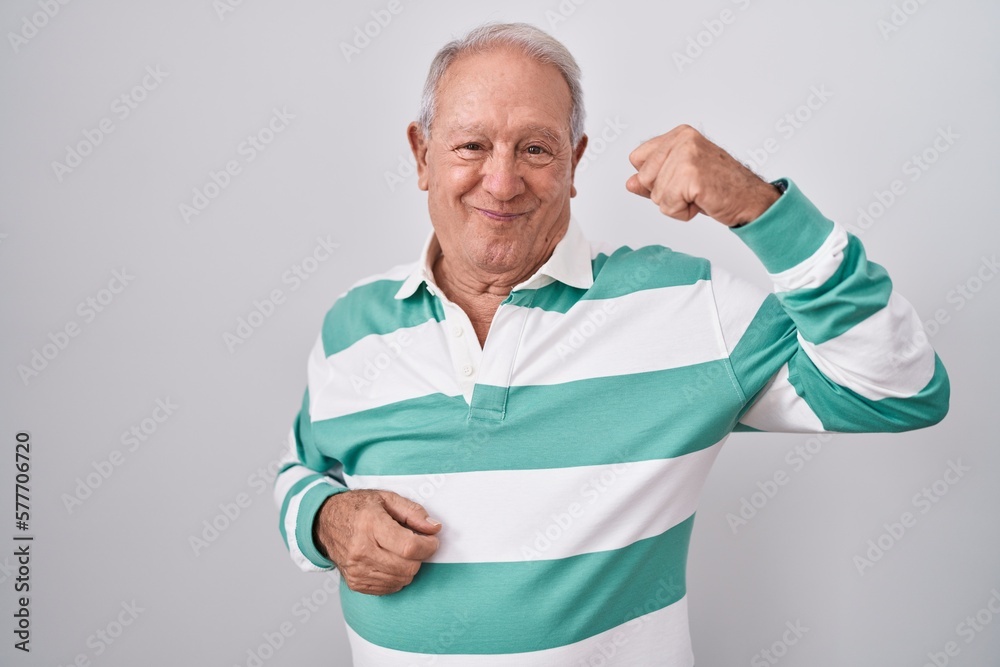 Senior man with grey hair standing over white background strong person showing arm muscle, confident and proud of power Senior man with grey hair standing over white background strong person showing arm muscle, confident and proud of power