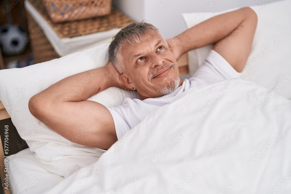 Middle age grey-haired man smiling confident lying on bed at bedroom