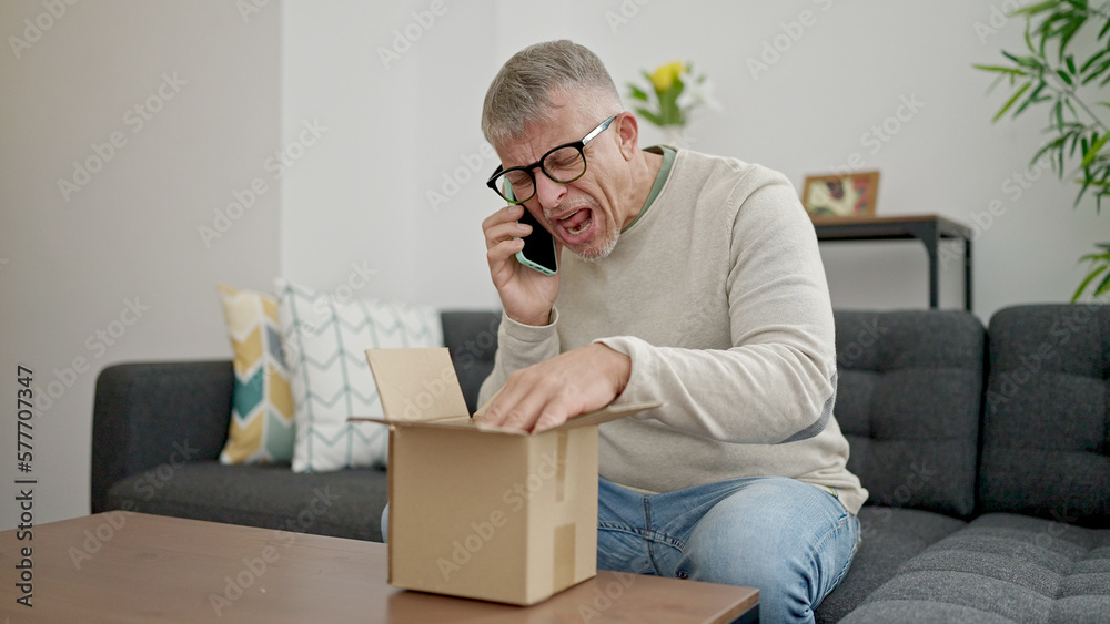 Middle age grey-haired man talking on smartphone arguing for package at home Middle age grey-haired man talking on smartphone arguing for package at home