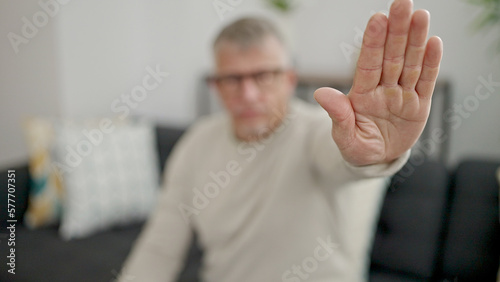 Middle age grey-haired man doing stop gesture with hand at home