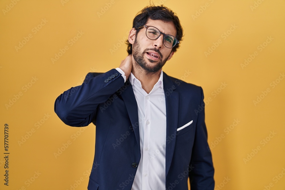 Handsome latin man standing over yellow background suffering of neck ache injury, touching neck with hand, muscular pain Handsome latin man standing over yellow background suffering of neck ache injury, touching neck with hand, muscular pain