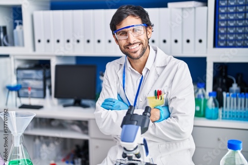 Fototapeta Naklejka Na Ścianę i Meble -  Young hispanic man scientist smiling confident with arms crossed gesture at laboratory