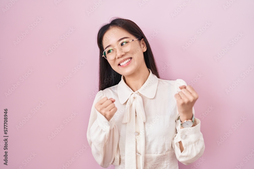 Young chinese woman standing over pink background very happy and excited doing winner gesture with arms raised, smiling and screaming for success. celebration concept. Young chinese woman standing over pink background very happy and excited doing winner gesture with arms raised, smiling and screaming for success. celebration concept.