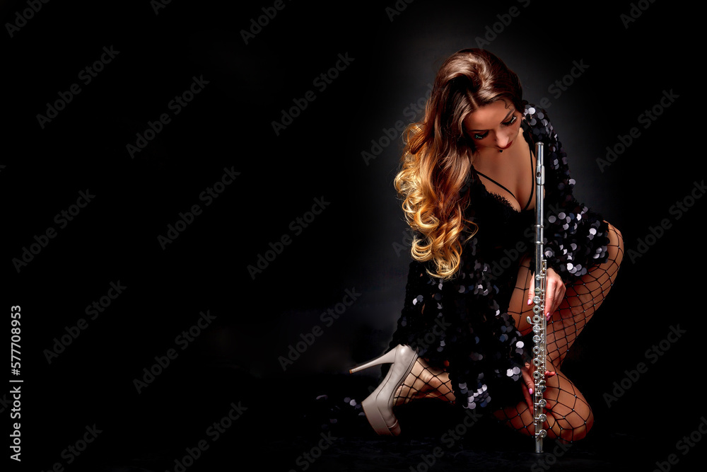 Sexy cover lady flautist posing with flute at black isolated background, looking at camera. Chic woman artist in black costume with flute in hands. Orchestra music concept. Copy text space, ad poster