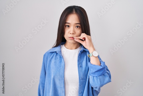 Young chinese woman standing over white background mouth and lips shut as zip with fingers. secret and silent, taboo talking photo