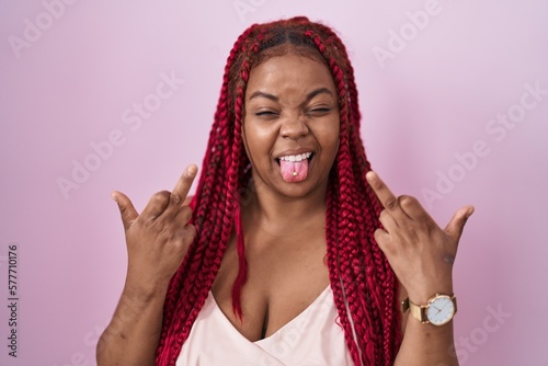 African american woman with braided hair standing over pink background showing middle finger doing fuck you bad expression, provocation and rude attitude. screaming excited photo
