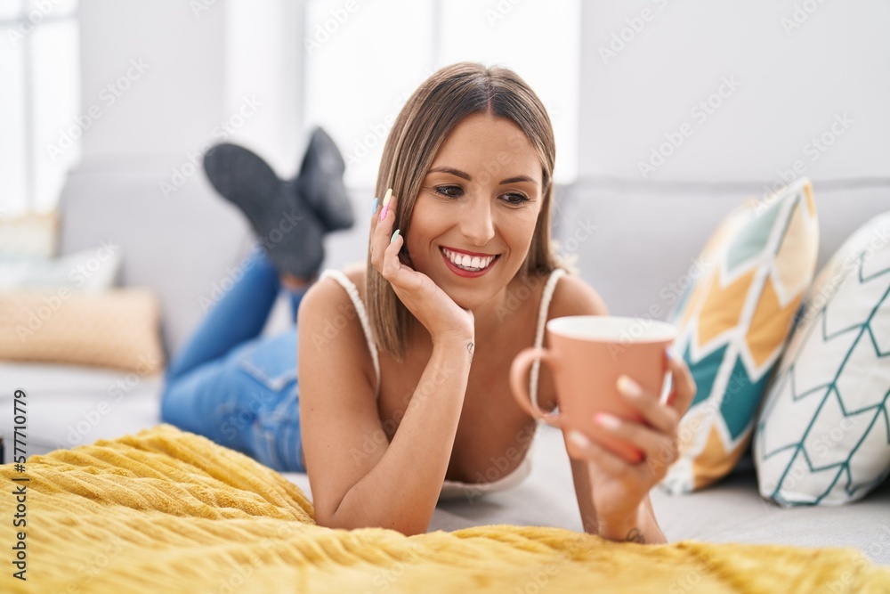 Young beautiful hispanic woman drinking coffee lying on sofa at home Young beautiful hispanic woman drinking coffee lying on sofa at home