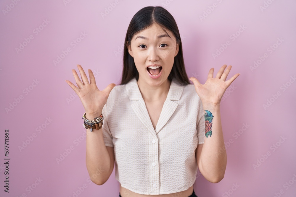 Chinese young woman standing over pink background celebrating crazy and amazed for success with arms raised and open eyes screaming excited. winner concept