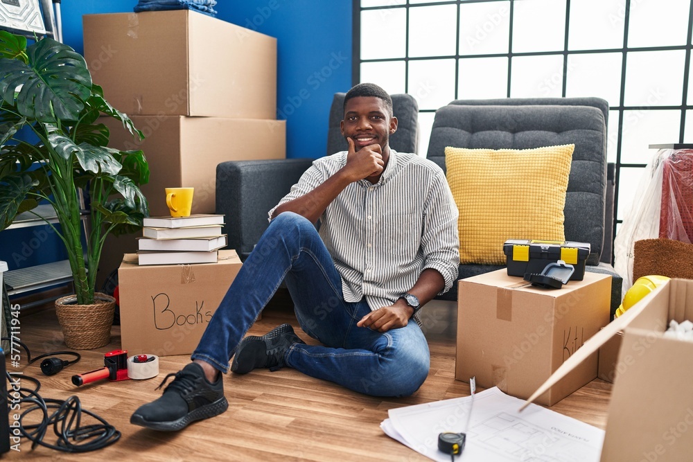 African american man sitting on the floor at new home looking confident at the camera smiling with crossed arms and hand raised on chin. thinking positive. African american man sitting on the floor at new home looking confident at the camera smiling with crossed arms and hand raised on chin. thinking positive.