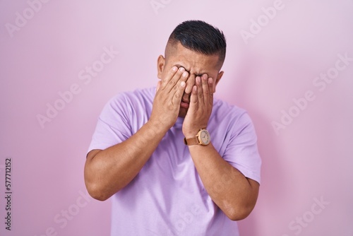 Young hispanic man standing over pink background rubbing eyes for fatigue and headache, sleepy and tired expression. vision problem