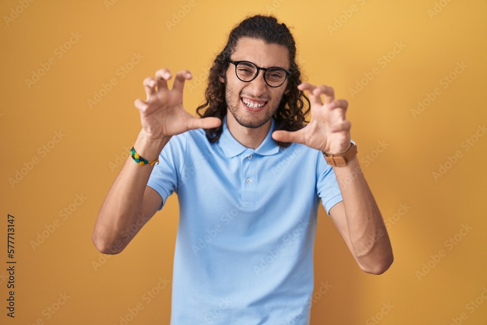 Fototapeta premium Young hispanic man standing over yellow background smiling funny doing claw gesture as cat, aggressive and sexy expression