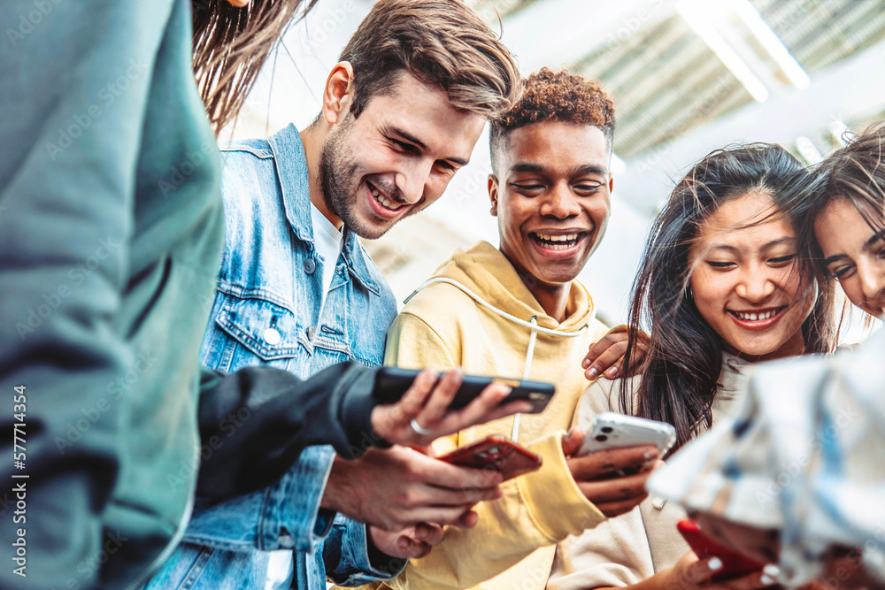 Fototapeta premium Diverse group of young people using smart mobile phone device outside - University students watching cellphone in college campus - Happy teenagers addicted to social media - Technology concept