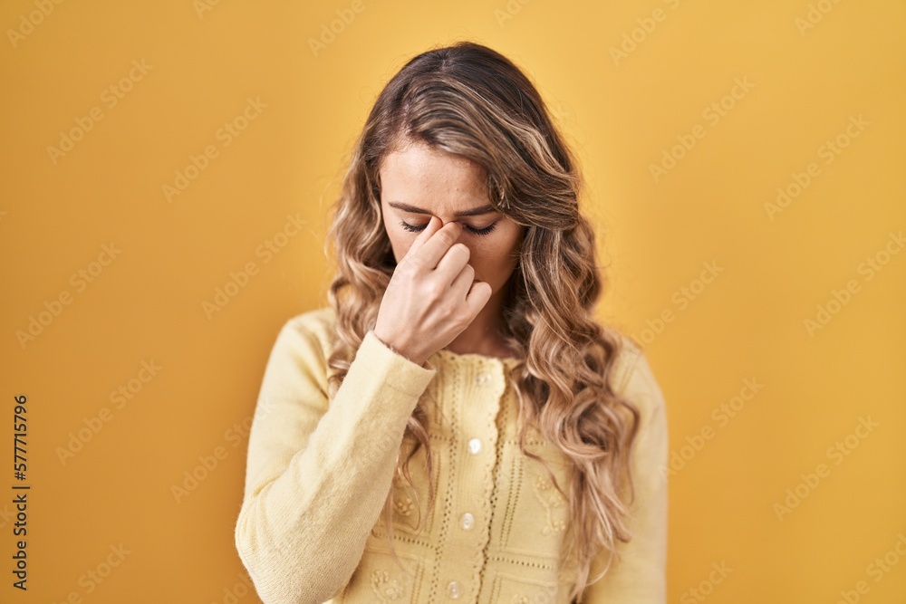 Young caucasian woman standing over yellow background tired rubbing nose and eyes feeling fatigue and headache. stress and frustration concept.