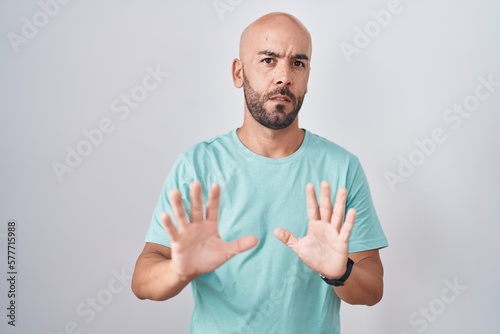 Middle age bald man standing over white background moving away hands palms showing refusal and denial with afraid and disgusting expression. stop and forbidden.