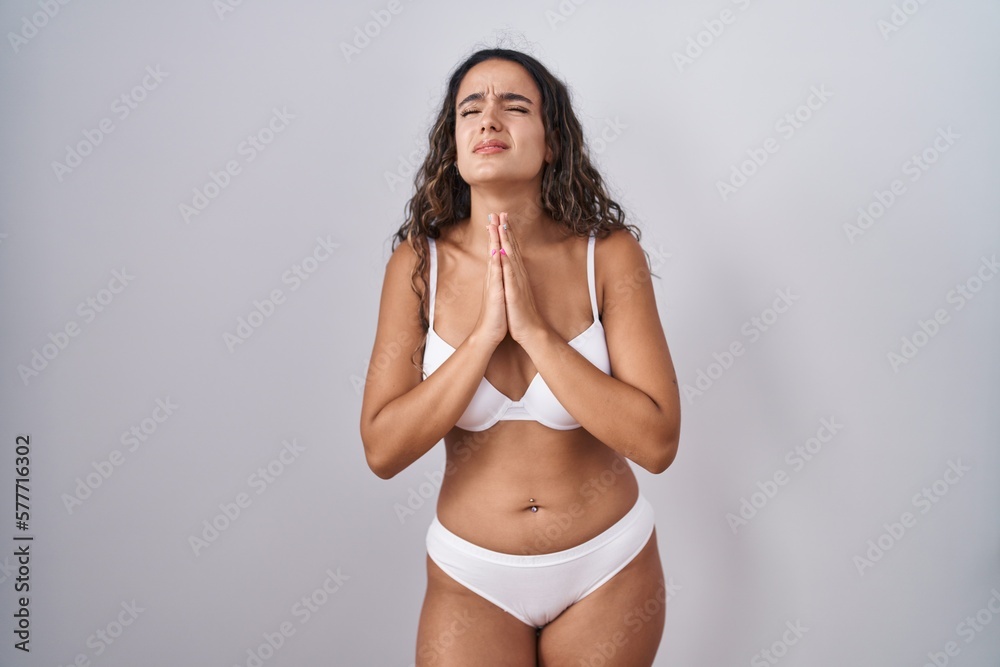 Fototapeta premium Young hispanic woman wearing white lingerie begging and praying with hands together with hope expression on face very emotional and worried. begging.