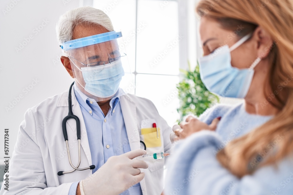 Middle age man and woman doctor wearing medical mask vaccinating patient at clinic Middle age man and woman doctor wearing medical mask vaccinating patient at clinic