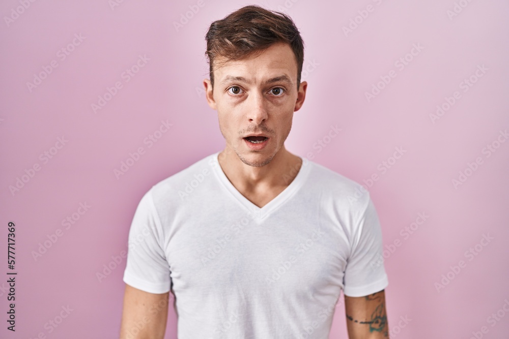 Caucasian man standing over pink background afraid and shocked with surprise and amazed expression, fear and excited face.