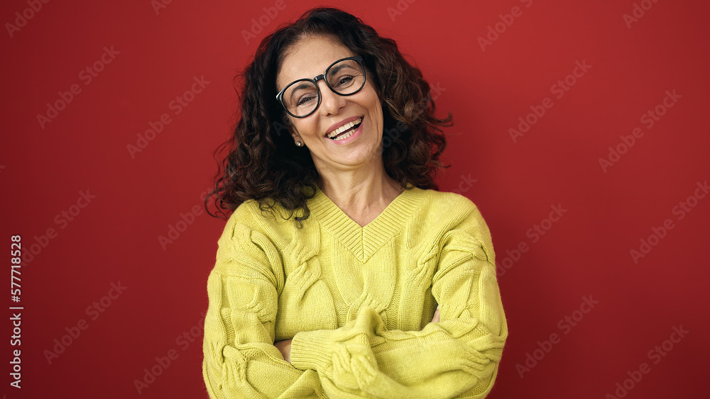 Middle age hispanic woman smiling confident standing with arms crossed gesture over isolated red background