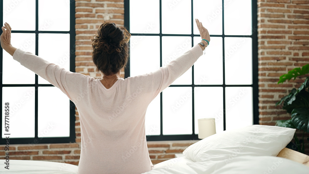 Middle age hispanic woman waking up stretching arms at bedroom