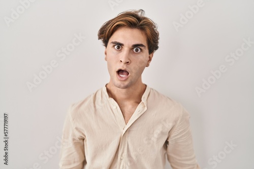 Young man standing over isolated background in shock face, looking skeptical and sarcastic, surprised with open mouth © Krakenimages.com