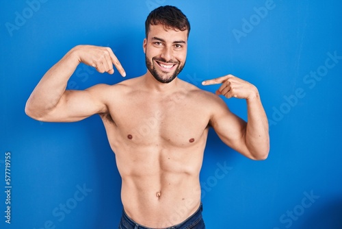 Handsome hispanic man standing shirtless looking confident with smile on face, pointing oneself with fingers proud and happy.