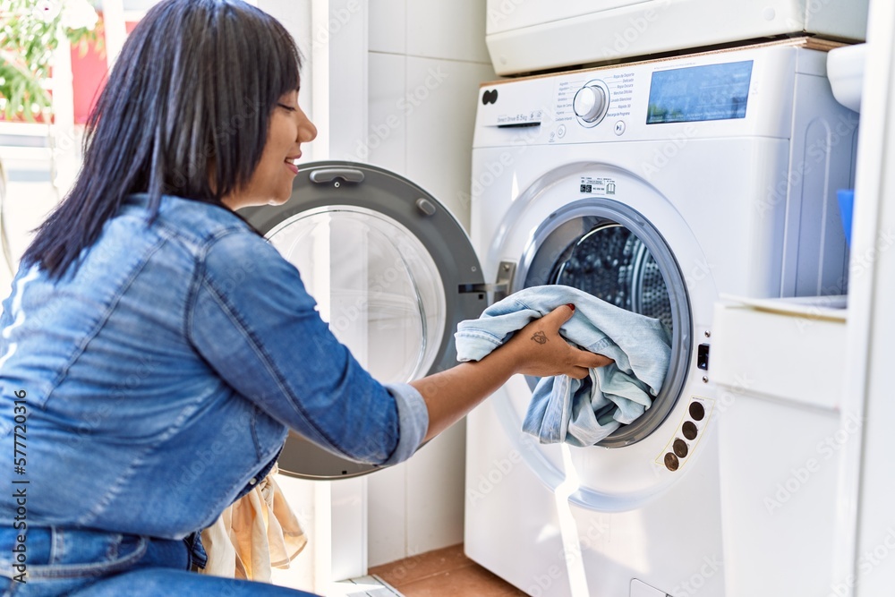 Hispanic brunette woman putting dirty laundry into washing machine at laundry room Hispanic brunette woman putting dirty laundry into washing machine at laundry room