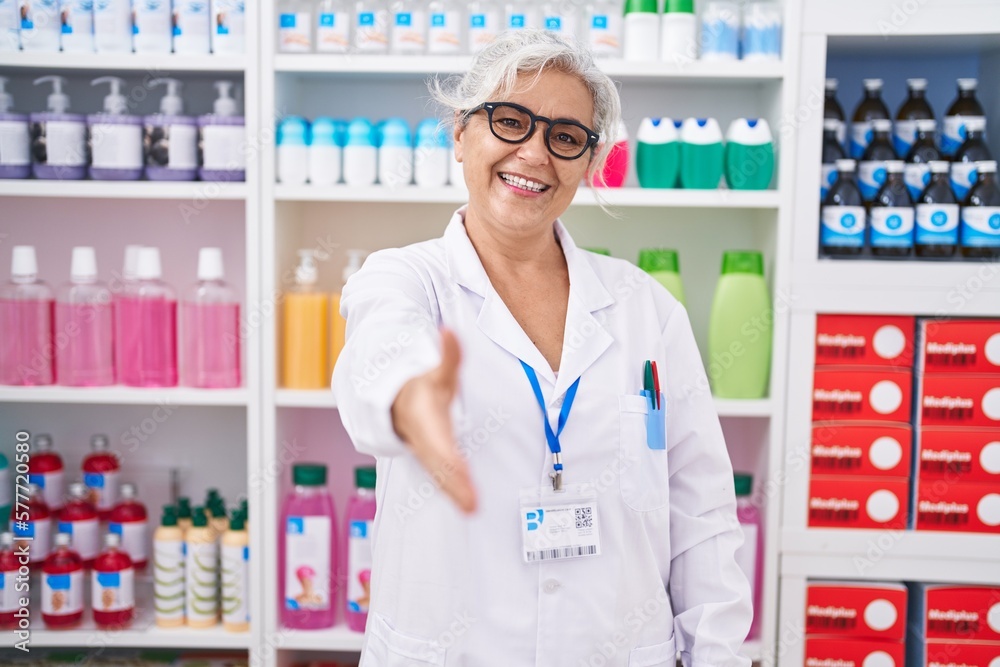 Middle age grey-haired woman pharmacist smiling confident shake hand at pharmacy Middle age grey-haired woman pharmacist smiling confident shake hand at pharmacy