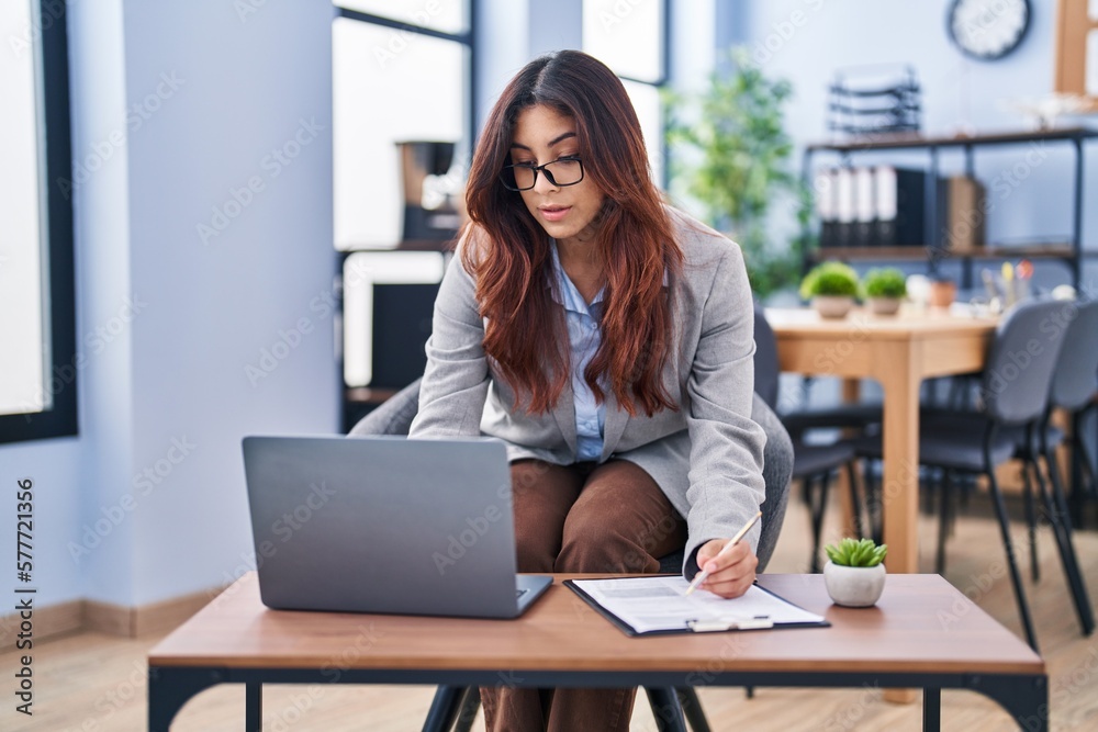 Young hispanic woman business worker using laptop write on document at office Young hispanic woman business worker using laptop write on document at office