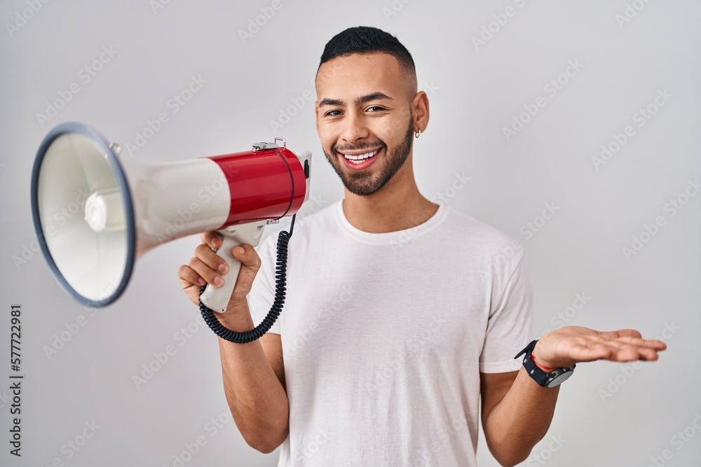 Young hispanic man shouting through megaphone celebrating achievement with happy smile and winner expression with raised hand Young hispanic man shouting through megaphone celebrating achievement with happy smile and winner expression with raised hand