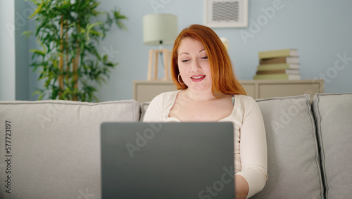 Young redhead woman using laptop sitting on sofa at home