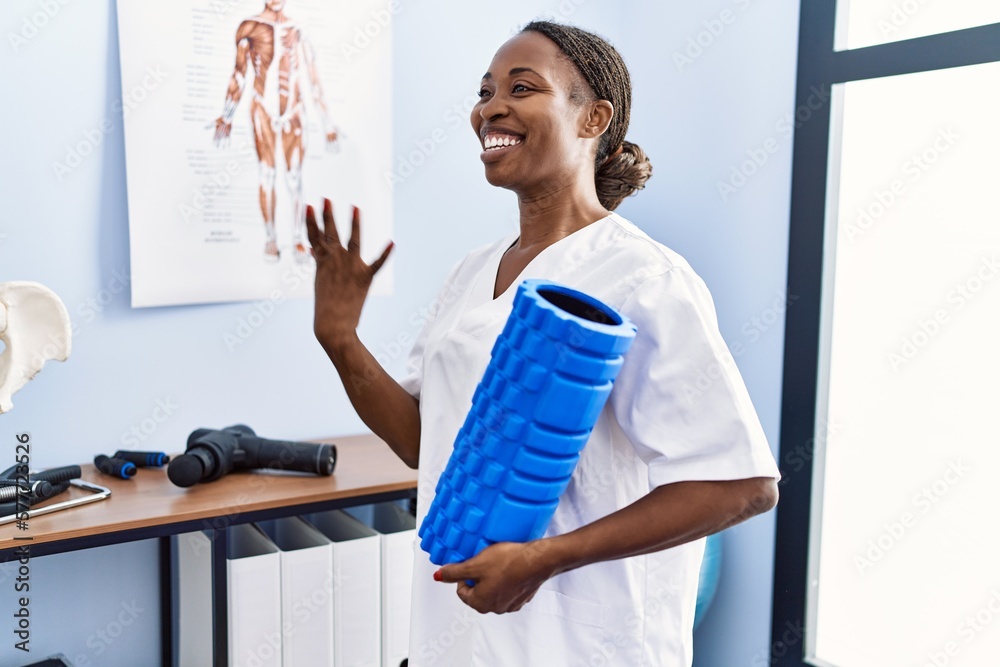 African american woman physiotherapist holding foam roller speaking at rehab clinic African american woman physiotherapist holding foam roller speaking at rehab clinic