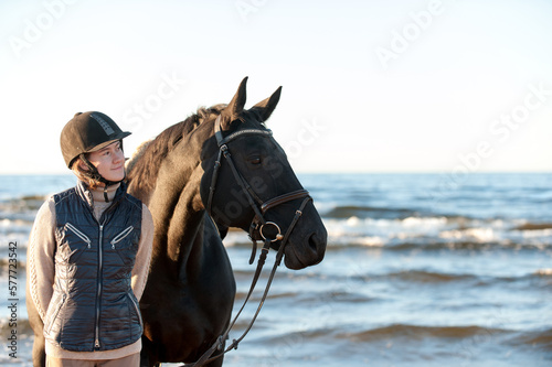 Young smiling Lady standing together with horse on sea beach